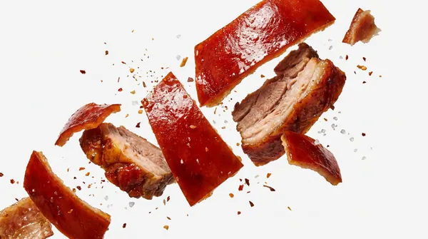 Cuts of Cebu lechon mid-air against a white ground