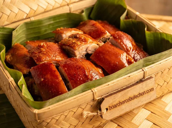 Cebu lechon pieces in a woven bamboo basket lined with banana leaf