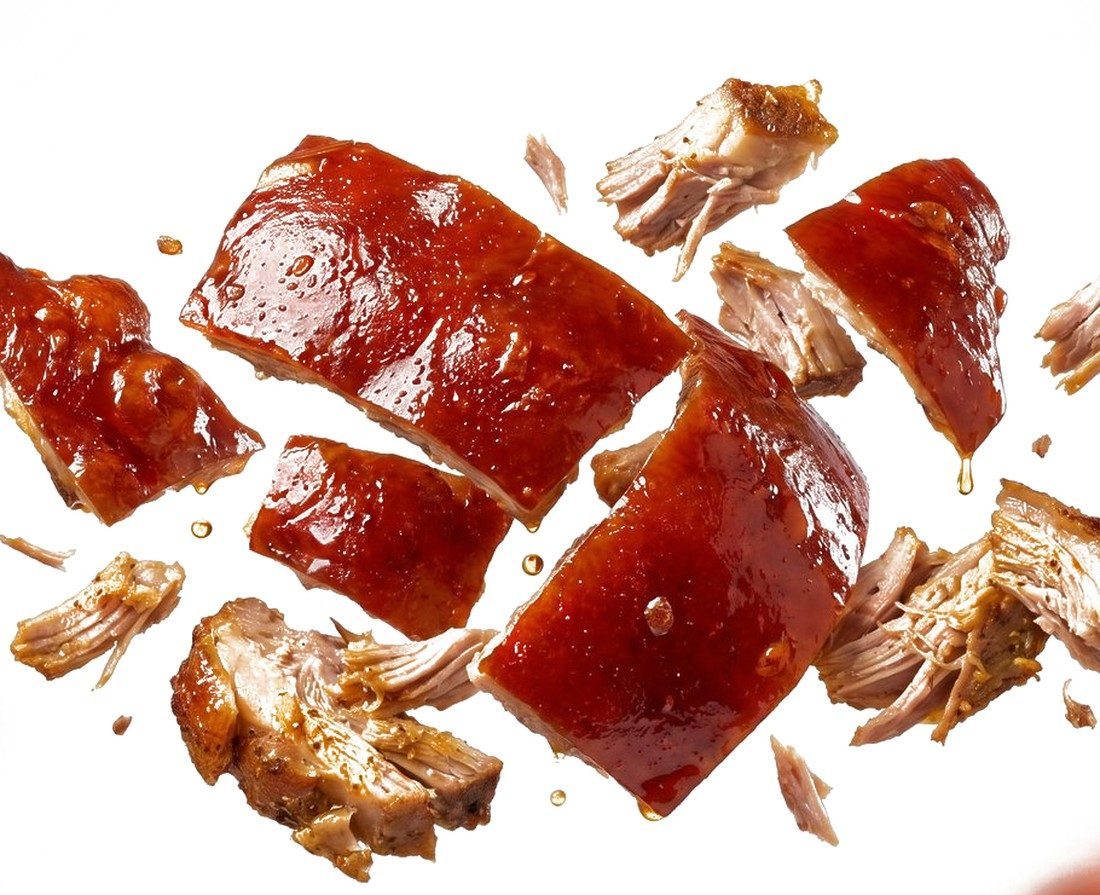 Pieces of Cebu lechon with crisp red skin falling through the air